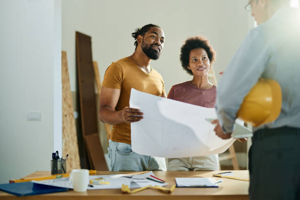 Happy African American couple analyzing blueprints while communicating with a building contractor